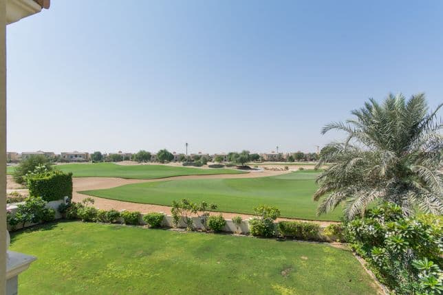 Scenic view of manicured fairways, sand bunkers, and palm trees from the backyard of a golf-facing villa.