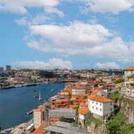 Malerischer Blick auf eine Flussstadt mit roten Dächern, einem fließenden Fluss, Booten und einem teilweise bewölkten Himmel.