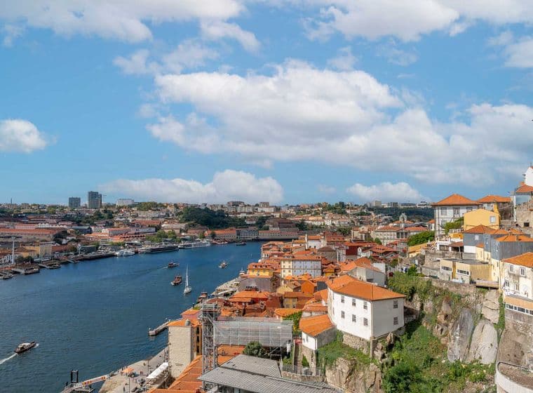 Malerischer Blick auf eine Flussstadt mit roten Dächern, einem fließenden Fluss, Booten und einem teilweise bewölkten Himmel.