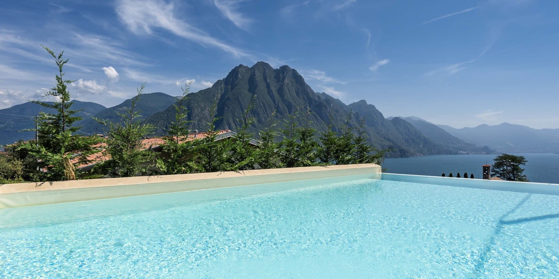 Infinity-Pool mit malerischer Aussicht auf Berge und einen See unter einem klaren blauen Himmel.