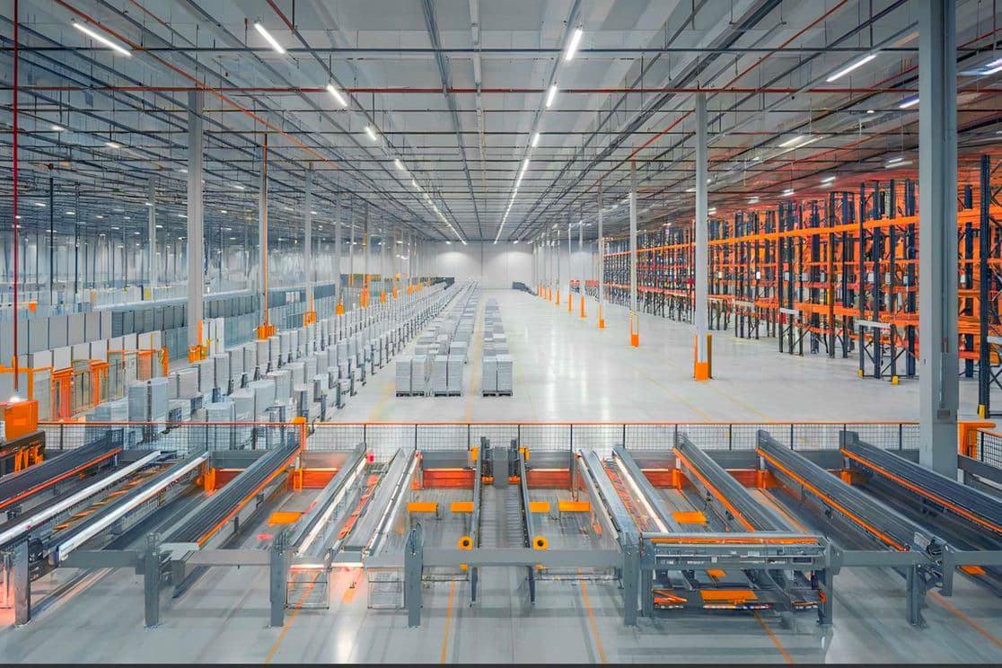 Vast modern warehouse interior with conveyor belts, empty shelving units, and bright overhead lighting.
