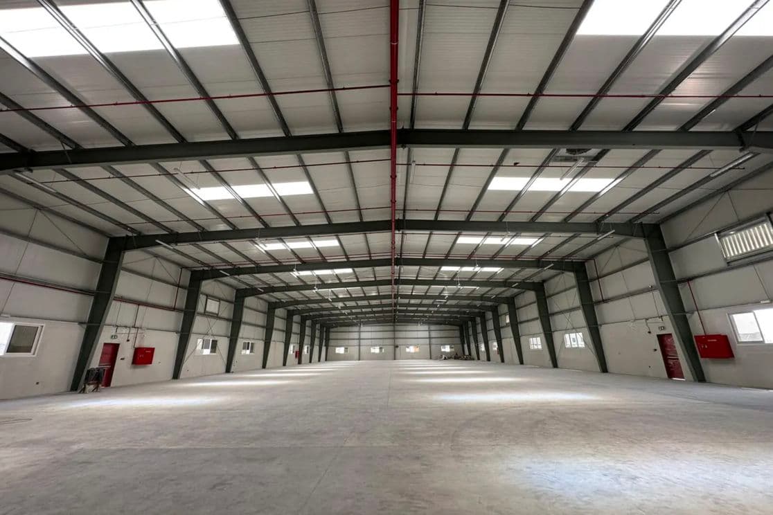 Spacious, empty warehouse interior with high ceiling, skylights, and visible structural beams. Fire safety equipment is mounted on the walls.