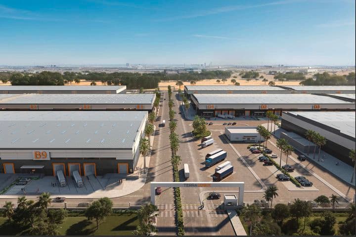Aerial view of a modern industrial park with large warehouse buildings, trucks, parked cars, and a central entrance gate marked "TERRA LOGYX."