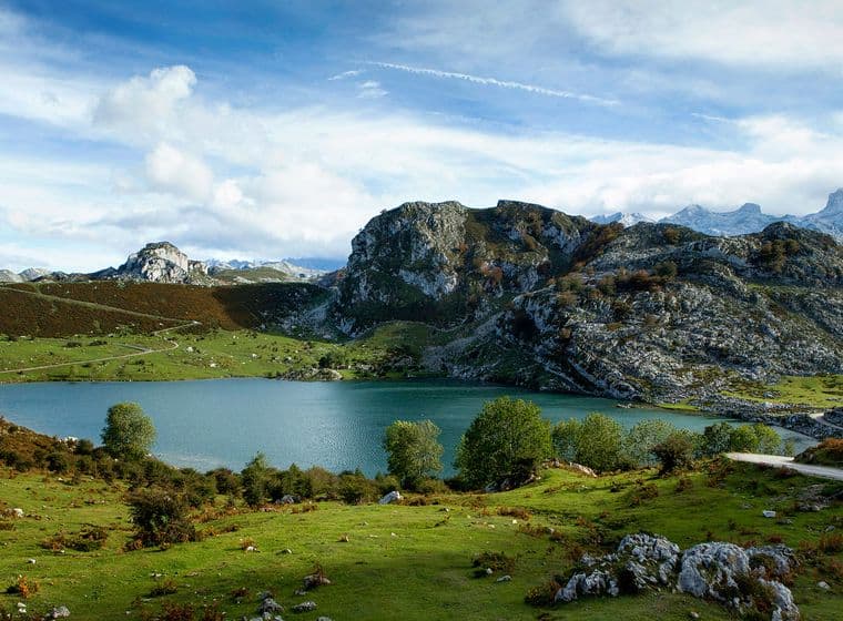 Vista panoràmica d'un llac blau envoltat de turons verds i muntanyes rocoses sota un cel ennuvolat.