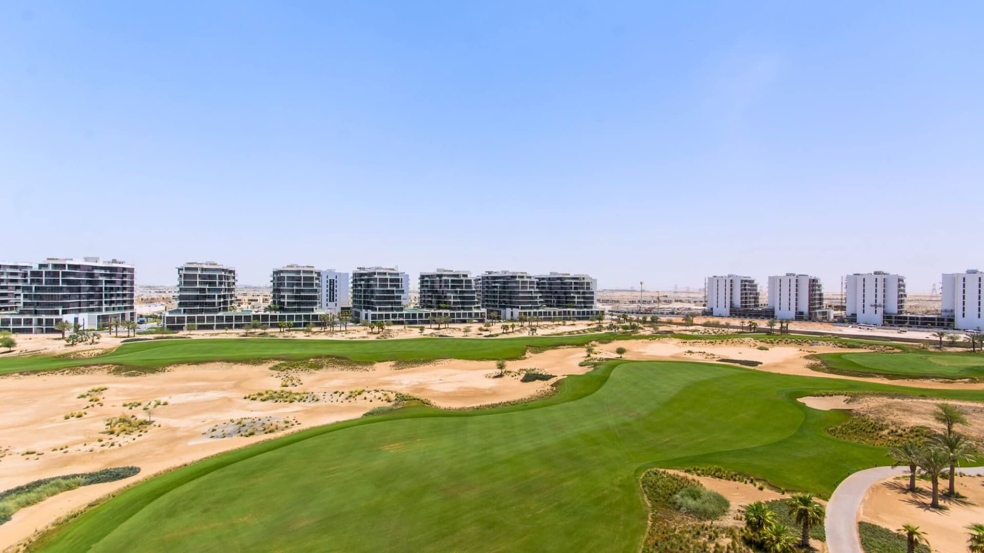 Aerial view of Damac Hills golf course with lush green fairways, surrounded by modern apartment buildings under a clear blue sky.