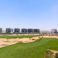 Aerial view of Damac Hills golf course with lush green fairways, surrounded by modern apartment buildings under a clear blue sky.