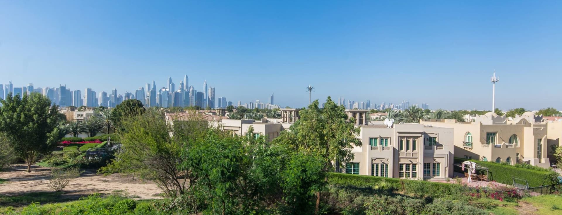 Aerial view of Jumeirah Park with lush greenery, set against a backdrop of a distant city skyline under a clear blue sky.
