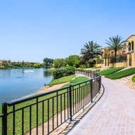 Waterfront property with a brick path, black railing, and yellow buildings. Palm trees and green landscaping add to the serene scene.