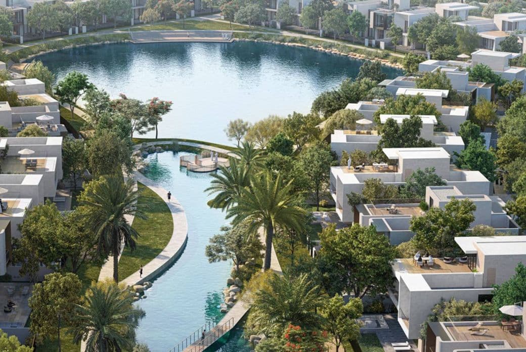 Aerial view of a residential area with modern houses, lush greenery, and a central circular lake connected by a narrow waterway.
