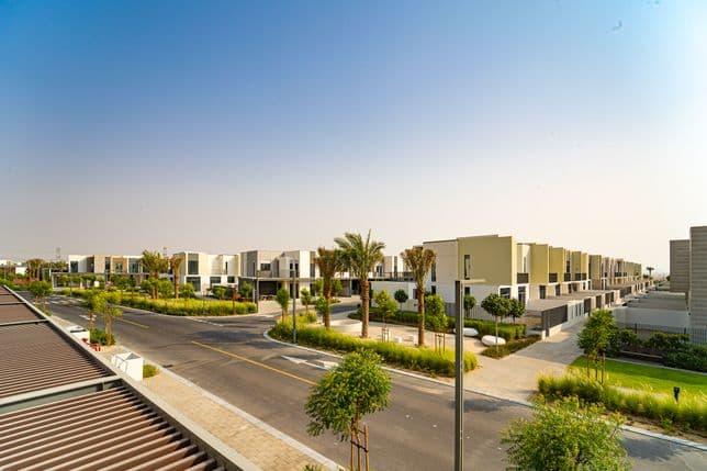 Elevated view of a wide residential street in Arabian Ranches 3 surrounded by modern villas, neatly trimmed greenery, and palm trees on a sunny afternoon.