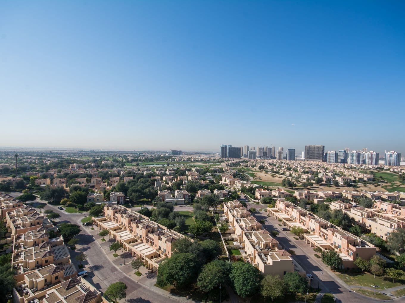 Panoramic view of Victory Heights showing rows of villas, tree-lined streets, and Dubai Sports City skyline in the distance.