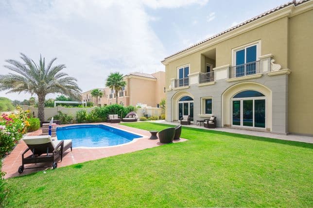 Spacious backyard with a blue-tiled pool, sun loungers, manicured lawn, and outdoor seating overlooking a two-storey villa.
