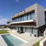 Casa moderna amb piscina. La casa té un exterior de formigó i grans finestrals. Hi ha una gespa verda i un cel blau.