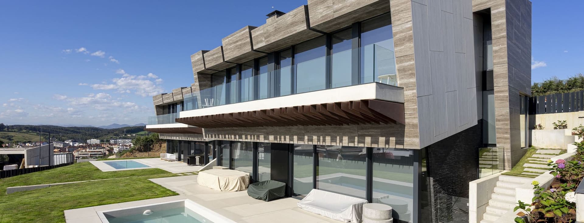 Modernes Haus mit Pool. Das Haus hat eine Betonfassade und große Fenster. Es gibt einen grünen Rasen und blauen Himmel.