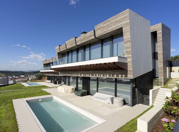 Modernes Haus mit Pool. Das Haus hat eine Betonfassade und große Fenster. Es gibt einen grünen Rasen und blauen Himmel.