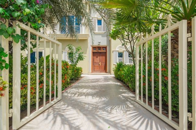 Gated pathway lined with tropical plants and flowers leading to a wooden front door of a villa in Victory Heights.