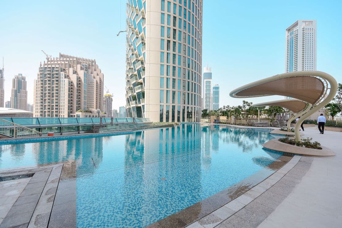 Outdoor swimming pool at Burj Vista in Dubai with a view of nearby towers and a shaded seating structure under a clear blue sky.