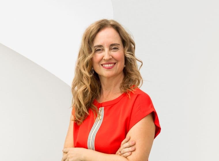 Smiling woman with long curly hair in a red dress stands against a white abstract background.