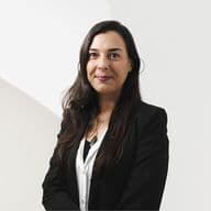 Woman in a black blazer and white shirt smiling against a minimalistic white background.