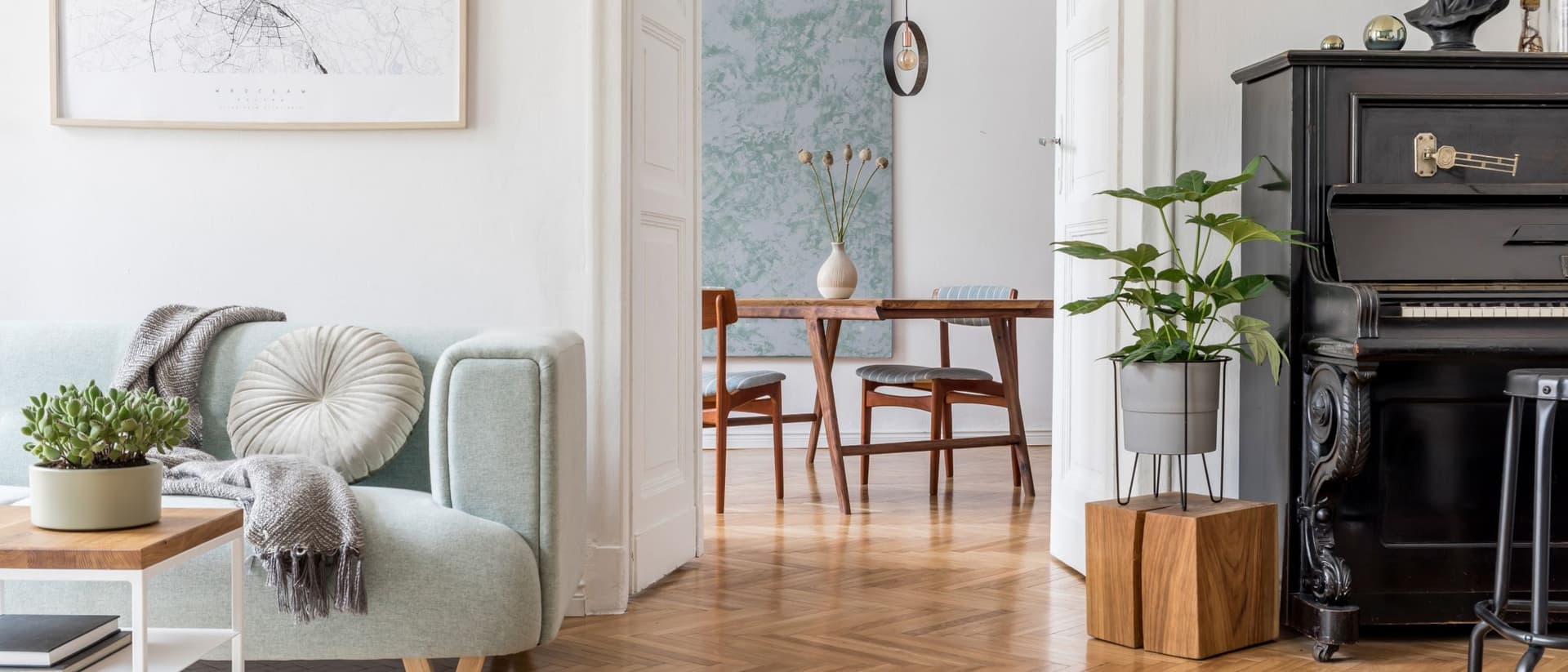 Se ve el interior de un apartamento con parquet en espiga , un sofa color verde lago a la izquierda, un piano negro a la derecha y en el centro, dos puertas abiertas dando al comedor con una mesa de madera oscura con dos sillas