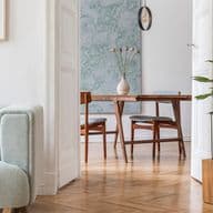 Espace de vie lumineux et ouvert, décoré dans un style scandinave avec un fauteuil vert pastel et des coussins décoratifs, des œuvres d'art murales abstraites, un piano noir vintage, des meubles de salle à manger en bois et un parquet à chevrons, présentant un mélange parfait d'éléments modernes et classiques.