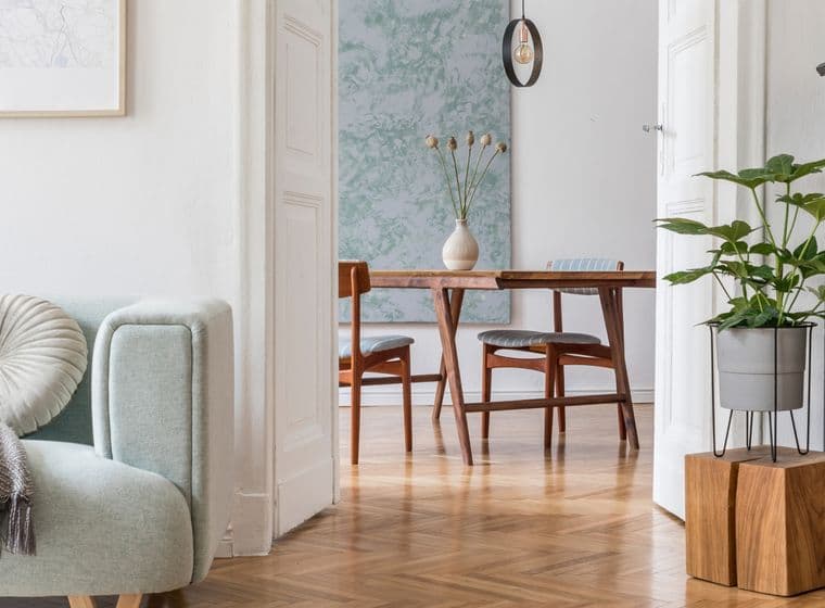 Heller, offener Wohnbereich im skandinavischen Stil mit einem pastellgrünen Loungesessel mit dekorativen Kissen, abstrakter Wandkunst, einem schwarzen Vintage-Klavier, hölzernen Esszimmermöbeln und Fischgrätparkettboden, der eine perfekte Mischung aus modernen und klassischen Elementen darstellt