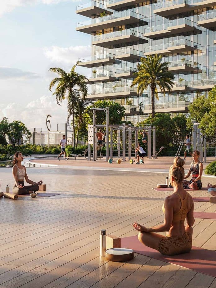 People practice yoga on mats outdoors near a modern building, surrounded by greenery and exercise equipment.