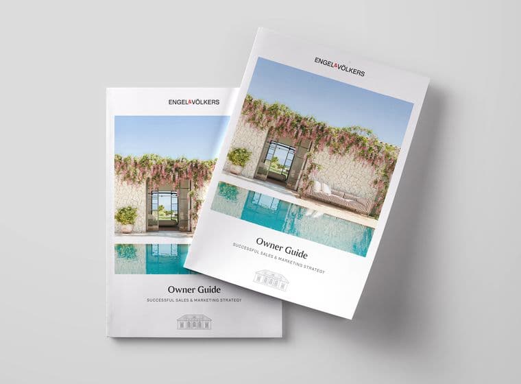 Two copies of the Engel & Völkers 'Owner Guide: Successful Sales & Marketing Strategy' brochure placed on a light grey surface. The cover features a luxurious poolside view with a stone wall, open doorway, flowering vines, and stylish outdoor furniture.