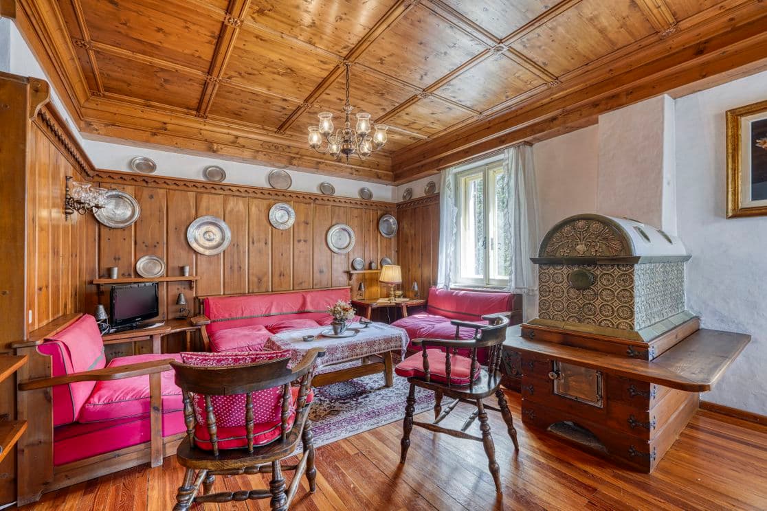 Gemütliches Wohnzimmer mit Holzvertäfelung, roten Sofas, verzierter Decke, dekorativen Tellern, einem Fernseher und einer Vintage-Truhe auf einem Holztisch.