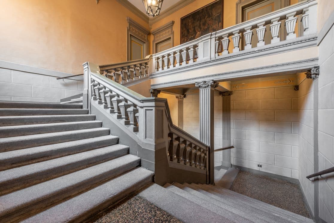 Elegante Innentreppe mit verzierten Geländern, Säulen und einer warmen, sanft beleuchteten Atmosphäre in einem historischen Gebäude.