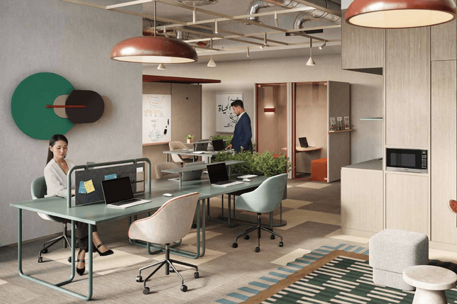 Open-plan office with people at desks, teal round wall art, copper pendant lamps, plants, and Arabic calligraphy on the wall.
