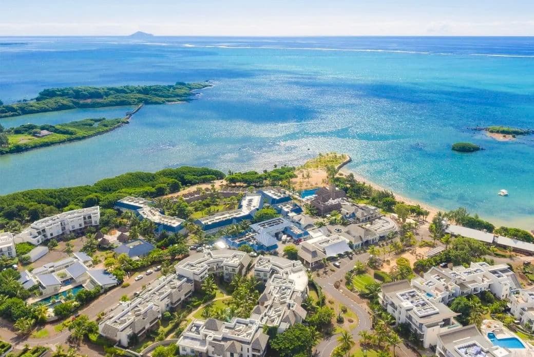 Aerial view of the coastal resort Haute Rive with white buildings, lush greenery, and turquoise ocean waters under a clear blue sky.