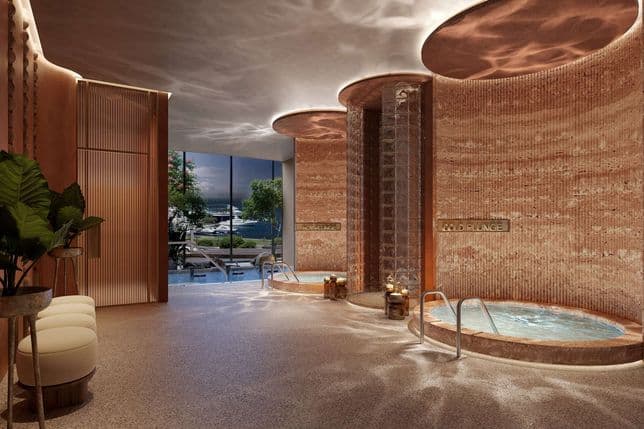 Luxurious spa with warm lighting, featuring hot and cold plunge pools, lush plants, and a view of a marina through large windows.