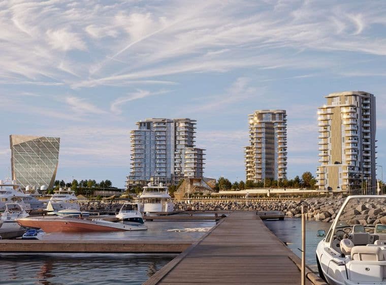 Marina with yachts, a dock, and modern high-rise buildings under a partly cloudy sky. Palm trees line the waterfront.