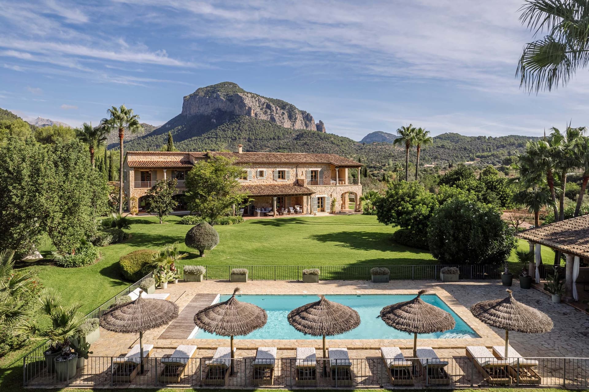The luxurious villa with pool, sun loungers, and umbrellas, nestled in the lush garden with mountain views in the background.