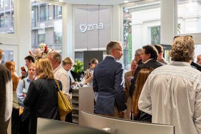 A group of people engaged in conversation at a well-lit indoor event space, featuring modern decor and floral arrangements.