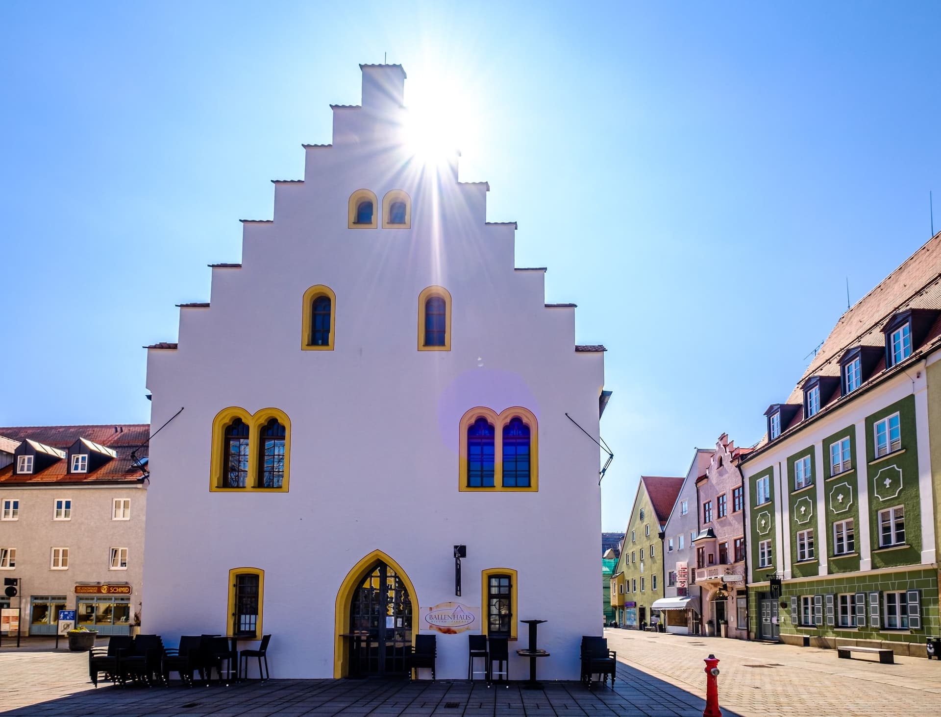 White historic building with stepped gable and yellow window frames in the center of Schongau’s old town, surrounded by cobblestone streets and colorful houses