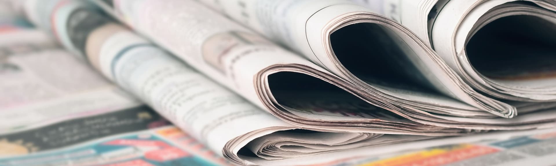 Nahaufnahme von gestapelten Zeitungen mit sichtbarem Text und Bildern, was auf einen Schwerpunkt auf Nachrichten und Informationen hindeutet.