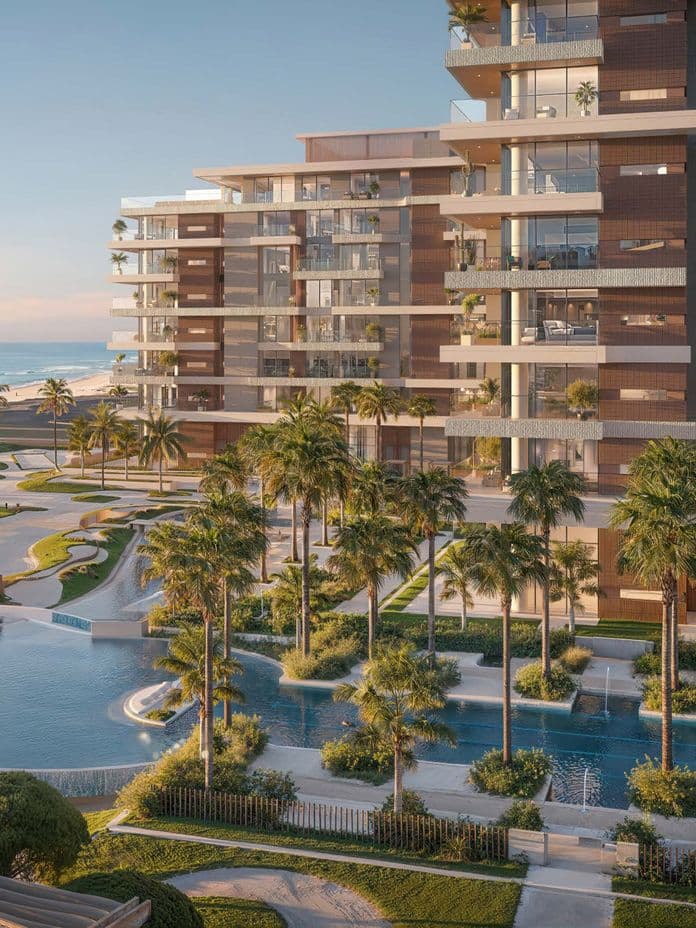 A modern beachfront residential development with glass-fronted balconies overlooking landscaped pools, palm trees, and a sandy shoreline along calm blue water at sunset.