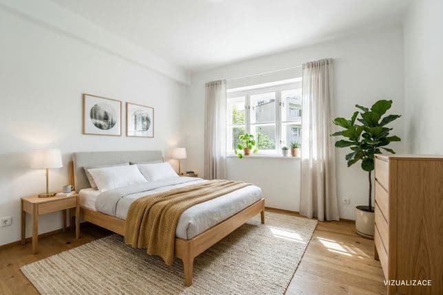 Cozy bedroom with a double bed featuring a wooden frame, two bedside tables with lamps and a light rug. Plants are placed by the window with sheer curtains, while a chest of drawers and a tall indoor plant stand on the right. The space feels airy and is filled with natural daylight.