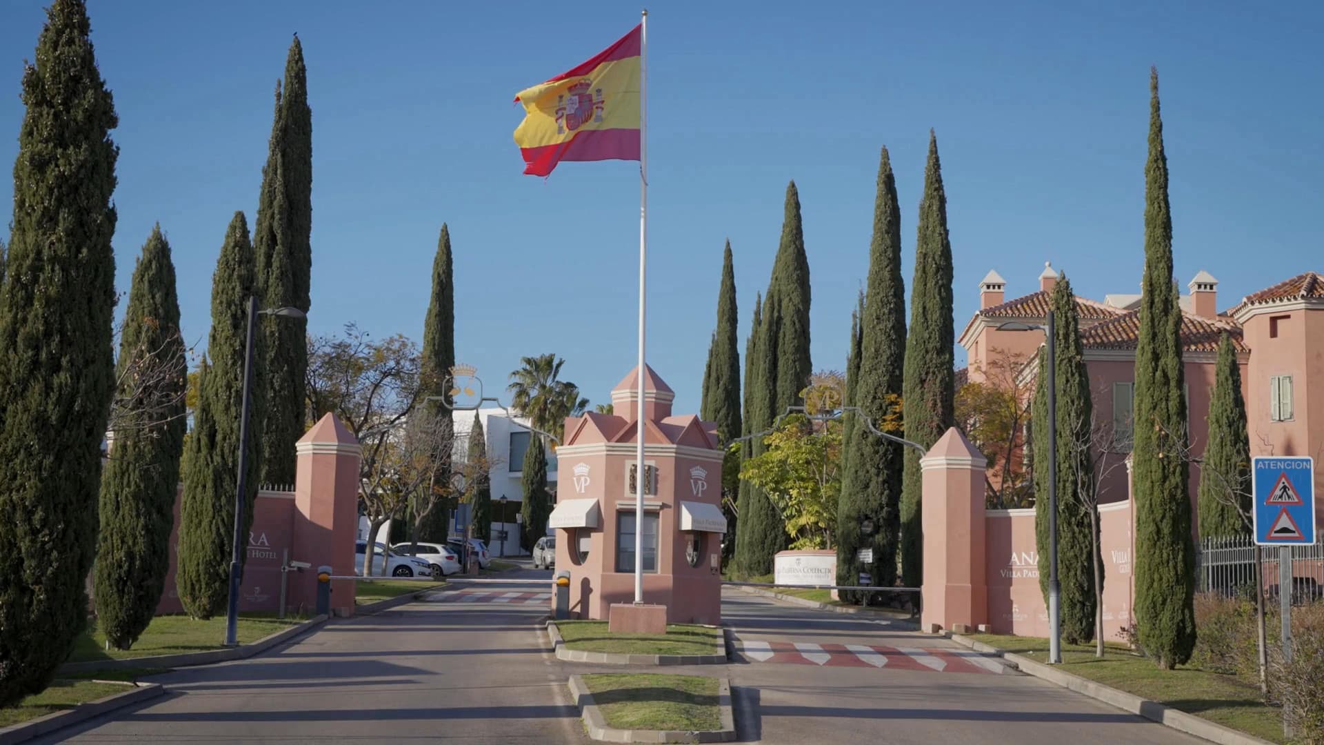 Entrada a Los Flamingos Golf amb edificis de color rosa i una bandera espanyola.