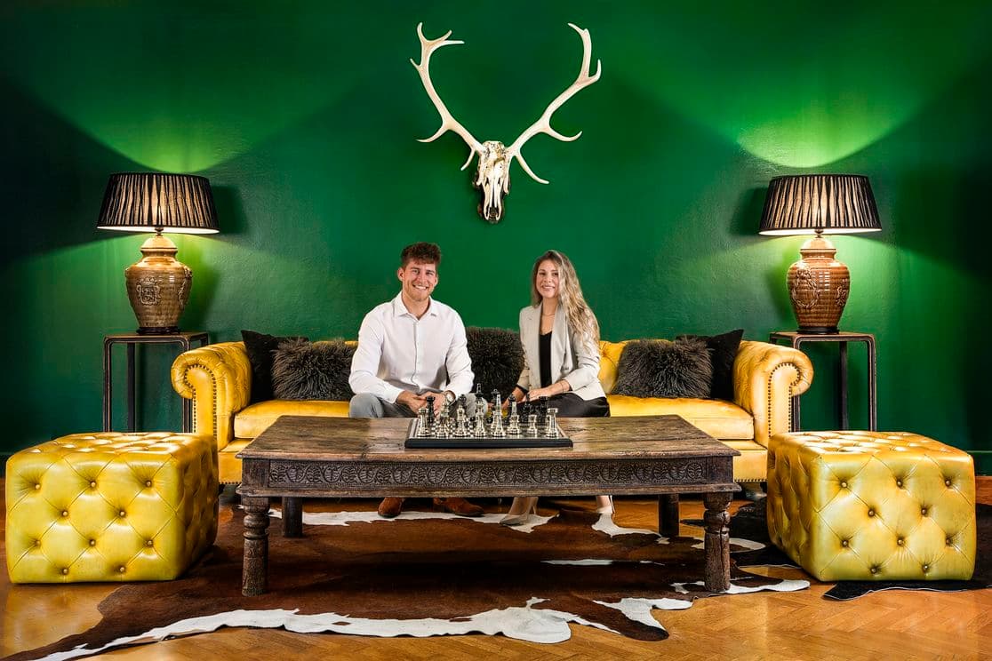 Elegantes Interieur mit grüner Wand, gelbem Chesterfield-Sofa, Schachspiel auf antikem Tisch und dekorativem Geweih