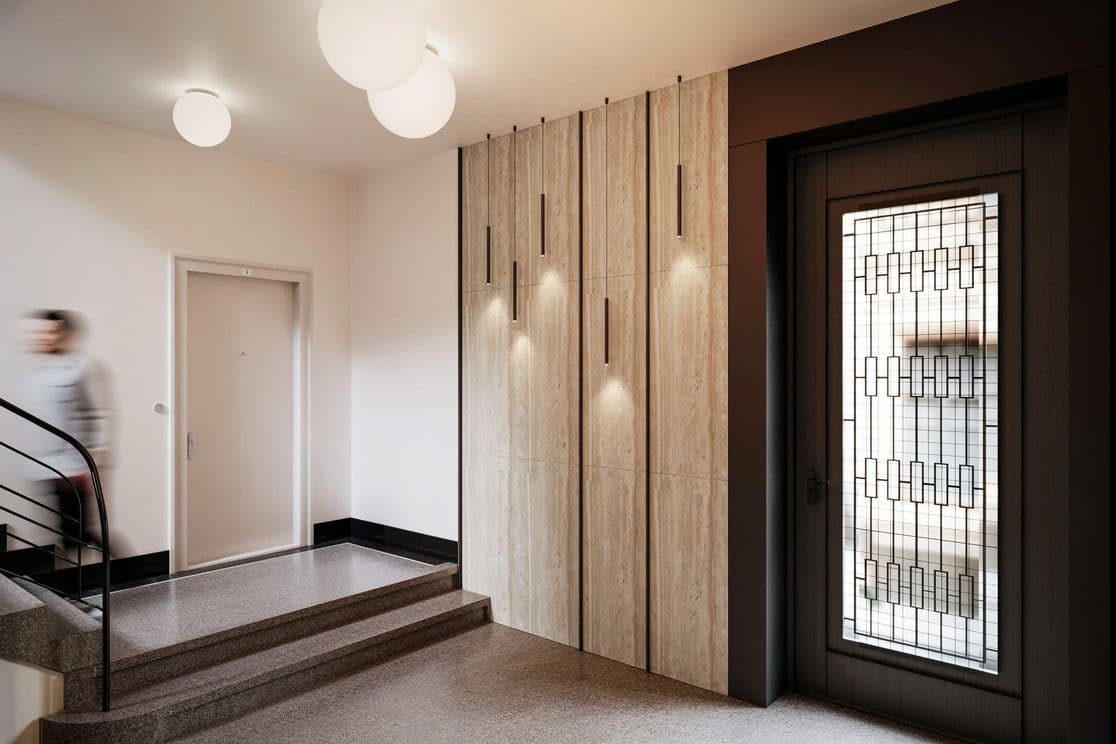 Hallway with staircase and entrance door featuring a geometric glass panel, wooden wall cladding with integrated lighting, and round ceiling lights.        Zeptat se služby ChatGPT