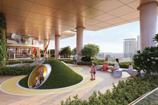 Children playing on a rooftop playground with slides and artificial hills, while adults sit nearby under a modern architectural canopy with city views.