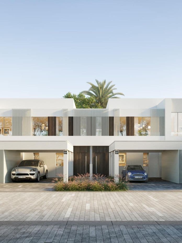 Modern white townhouse with large windows, two garages, and surrounded by lush greenery and palm trees under a clear blue sky.