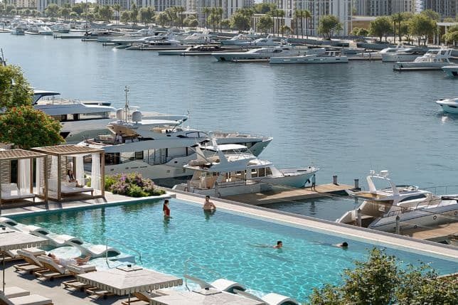 Luxury infinity pool next to yacht berths at Rashid Marina, with cabanas, sun loungers, and people enjoying the serene waterfront atmosphere.