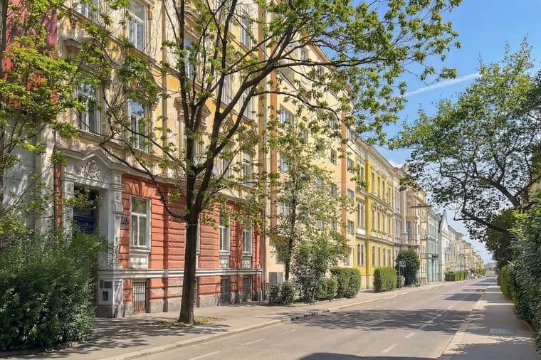 Street view of colorful European-style buildings with trees lining the sidewalk on a sunny day.