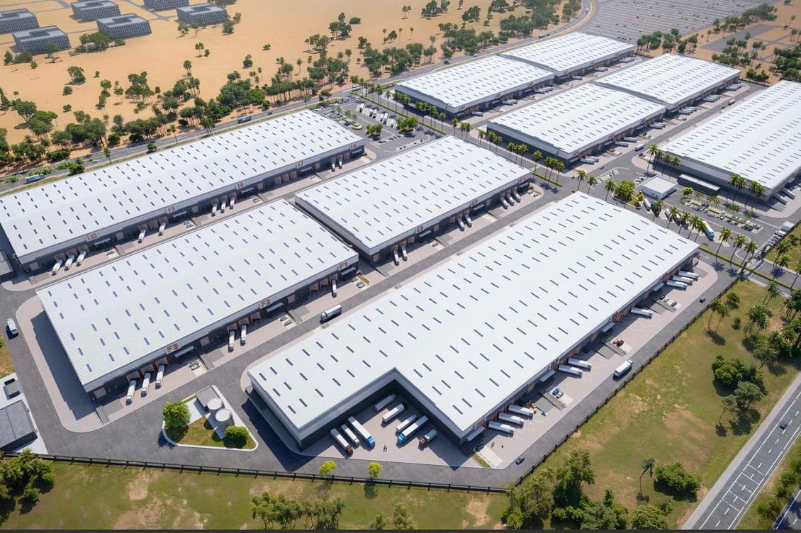 Aerial view of a large industrial complex with multiple white-roofed warehouses surrounded by greenery and roads.