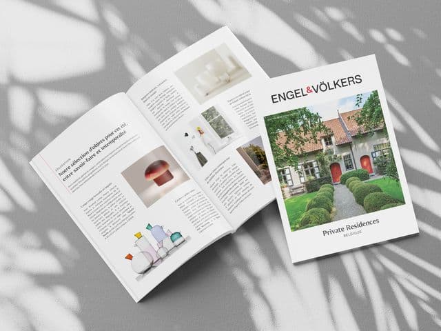 Open magazine with home decor images and text on a sunlit surface, next to a brochure titled "Private Residences Belgique."