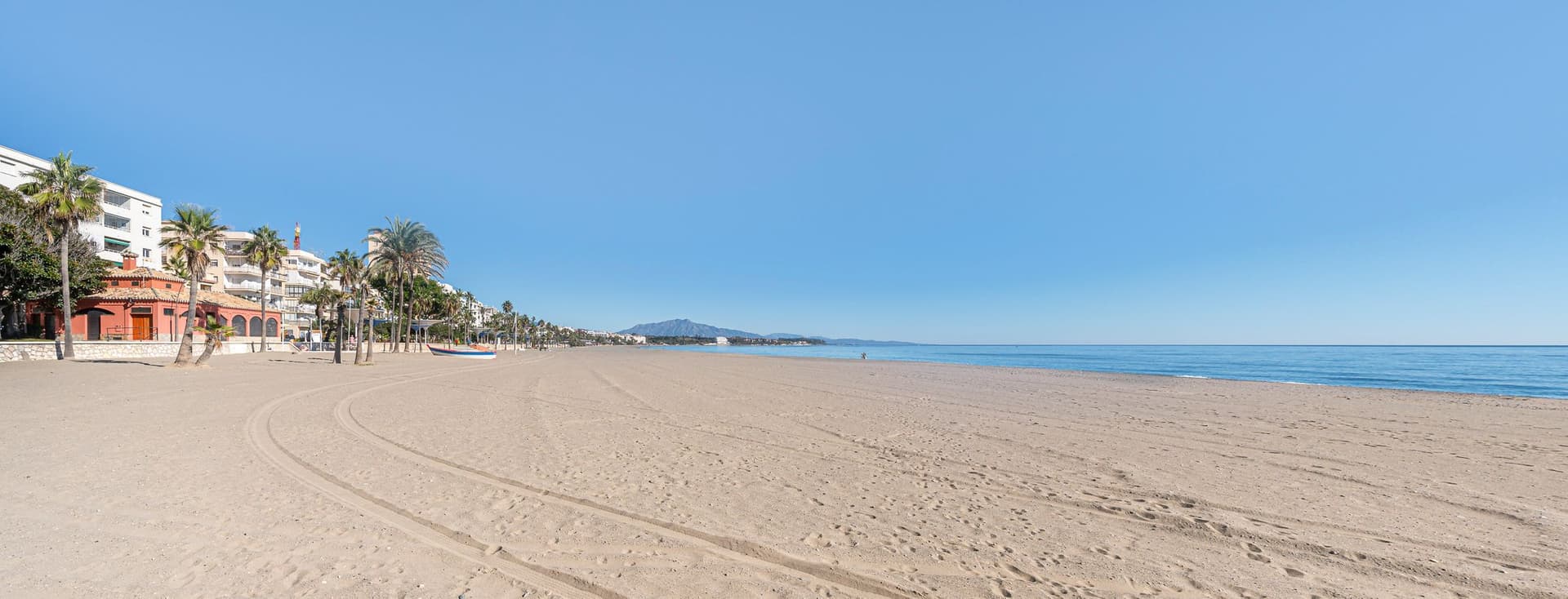 Platja d'Estepona amb palmeres i edificis. Sorra fina i el mar.